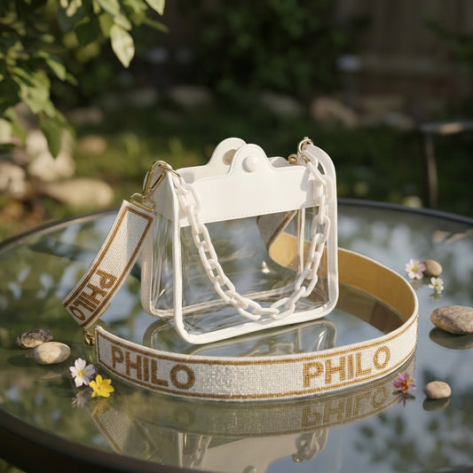 Miniature clear concert crossbody bag placed on a reflective glass table in a garden setting with natural light.