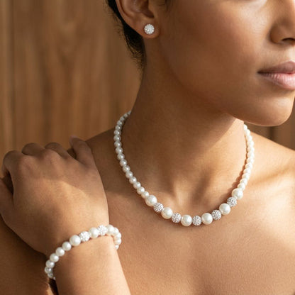 Delicate white pearl and clay shamballa jewelry set on a minority woman, featuring necklace, bracelet, and post earrings, displayed naturally.