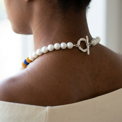 Close-up of the 14-foot necklace featuring white pearls and vibrant yellow and blue shamballa beads, with a silver toggle clasp on silk fabric.